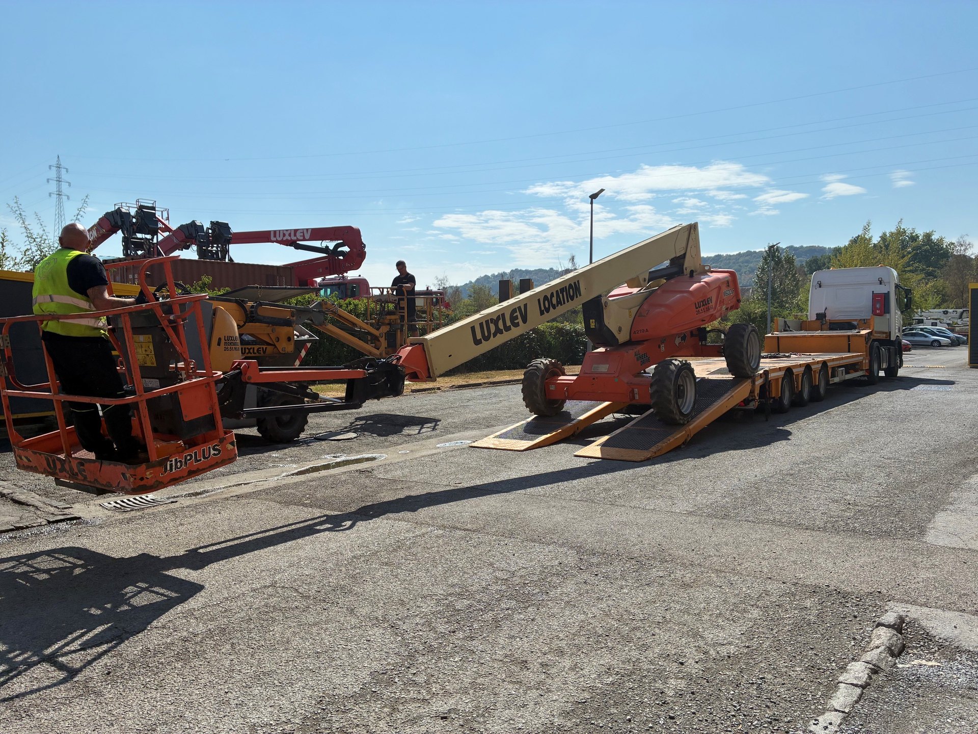 Équipe LUXLEV chargeant une nacelle articulée sur un porte-engins au dépôt de Pétange